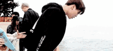 a young man in a black hoodie is bending over in front of the ocean .