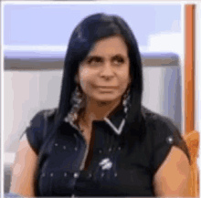 a woman with long black hair is wearing a black shirt and earrings and making a funny face .