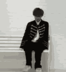 a man is sitting on a white bench wearing a black jacket and tie .