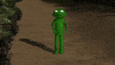 a green frog with white eyes is standing on a dirt road .