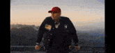a man wearing a red baseball cap and a black jacket is standing on a balcony .