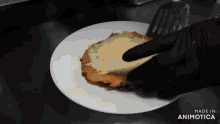 a person in black gloves is holding a piece of food on a plate that says made in animotica