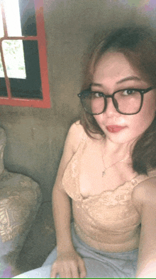 a woman wearing glasses and a bra takes a selfie in front of a window