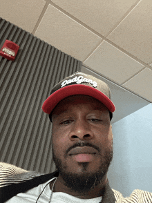 a man wearing a dad gang hat stands in front of a red fire alarm