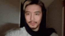 a man with a beard is wearing a scarf around his head and looking at the camera .