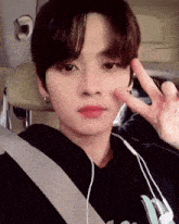 a young man is sitting in a car with headphones on and giving a peace sign .