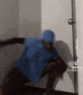 a man in a blue shirt and hat is standing in a room next to a door .
