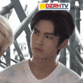 a young man in a white t-shirt is standing in front of a dzrhtv logo .