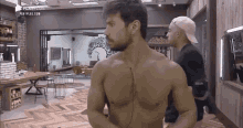 a man without a shirt is standing in a room next to two other men .