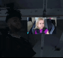 a little girl is sitting in a car seat next to a man in a black shirt
