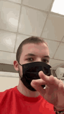 a man wearing a black face mask and a red shirt is giving a peace sign .