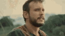 a man with a beard is standing in a field looking up at the sky .