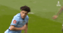 a soccer player is kneeling down on the field while another player kicks the ball .