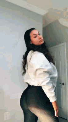 a woman is standing in a room wearing black leggings and a white sweatshirt .