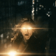 a woman is standing in the dark with a flash of light coming out of her eyes .