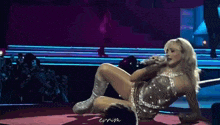 a woman is laying on the floor on a stage while holding a microphone .