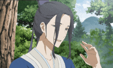 a man with long black hair and a blue shirt stands in front of a tree