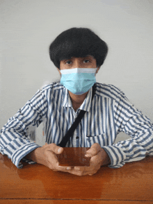 a man wearing a face mask sits at a table holding a card