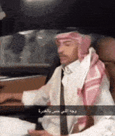 a man wearing a head scarf and a white shirt sitting in a car