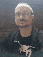 a man wearing glasses and a black shirt with a snake on it looks at the camera