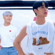 a man in a white tank top with a teddy bear on it is standing next to another man in a white shirt .