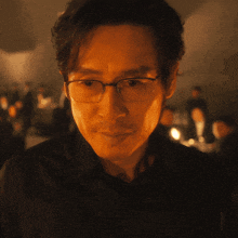 a man wearing glasses and a black shirt looks at the camera in a dark room