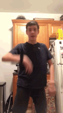 a young man in a black shirt is dancing in front of a fridge that has a yellow bag of ritz crackers on it