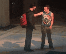 a man wearing a tank top with a bird on it stands next to another man with a backpack
