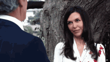 a man and a woman are standing next to a tree and the woman is smiling