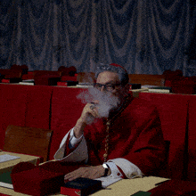 a man in a red robe is smoking a cigarette in a dark room
