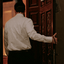 a man in a white shirt is standing in front of a wooden door