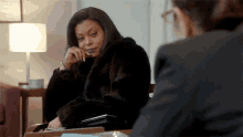 a woman in a fur coat is sitting at a table with a woman in a suit .