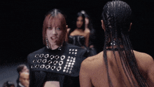 a woman wearing a black jacket with holes in it is standing next to another woman