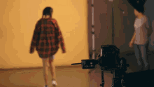 a woman in a plaid shirt is walking in front of a camera that says ' nikon ' on it