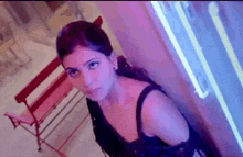 a woman in a black top is standing next to a red chair and looking at the camera .