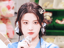 a girl in a blue shirt is holding a microphone with a heart in her hair clip
