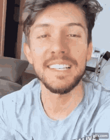 a man with a beard is smiling for the camera while wearing a blue shirt .