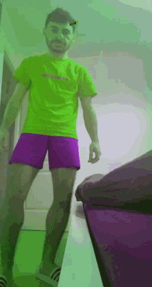 a man wearing a neon green shirt and purple shorts is standing next to a bed