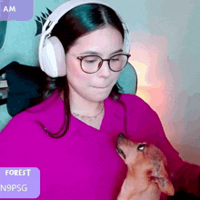 a woman wearing headphones and glasses holds a small dog in her arms