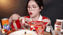 a woman wearing glasses is eating a cup of noodles with a fork and knife .