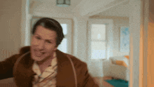 a man in a brown jacket is walking through a doorway in a living room .