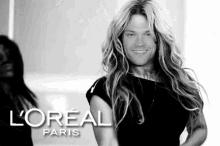 a man with long blonde hair is wearing a black dress and smiling in a black and white photo for loreal paris .
