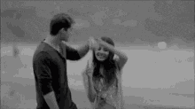 a black and white photo of a man and a woman dancing on the beach .