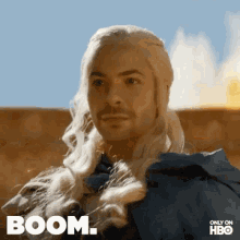 a man with long blonde hair is wearing a blue cape and has the word boom on his face .