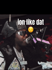 a man wearing sunglasses and a fur hat stands in front of a microphone with the words " ion like dat " above him