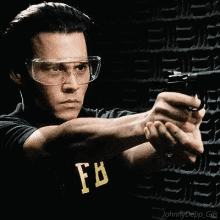 a man wearing goggles is pointing a gun at another man wearing a fb shirt