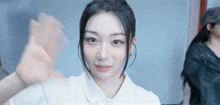 a woman in a white shirt is smiling and waving at the camera .