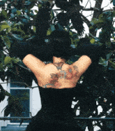 a woman with a tattoo on her back is standing in front of trees