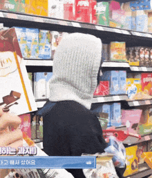 a woman wearing a hooded scarf is standing in front of a shelf with pepperoni on it