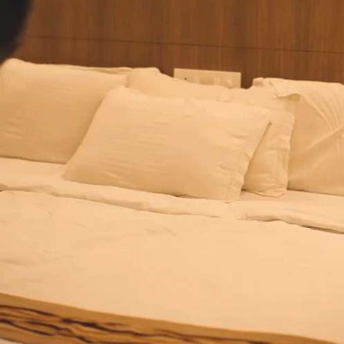 a bed with white sheets and pillows in a bedroom